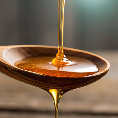 Wooden spoon with honey being dripped onto it against a blurred background