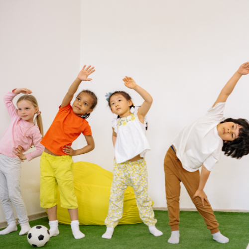 Four children posing energetically in a room with a green floor and white walls.
